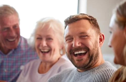 Senior Parents With Adult Offspring Sitting On Sofa At Home Talking And Laughing Stock Photos