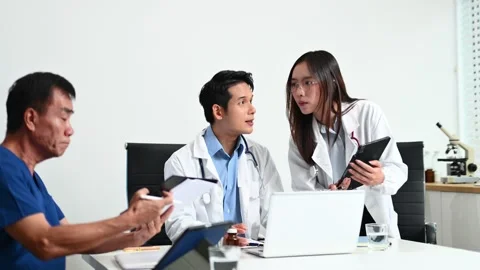 Senior patient meets with doctors using tablet and laptop in modern clinic... Video stock 313857897