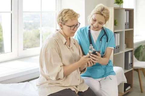Senior patient using smartphone with help of nurse, girl explaining digital app Foto stock