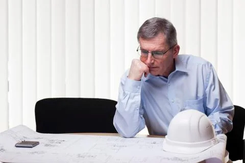 Senior pensive architect of engineer at a table with blueprint and white hard Stock Photos