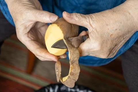 A senior person uses a small sharp knife to peel a fresh raw potato, showca.. Stock Photos