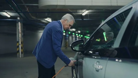 Senior is plugging in power cord to an electric car. 4K Video stock 72652575