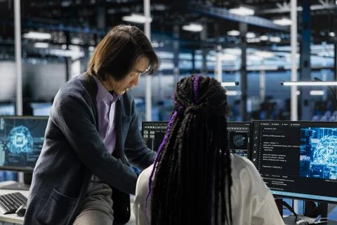 Senior programmer and trainee coding in diverse data center, updating AI scripts Stock-Fotos