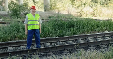 Senior railroader in uniform looking at camera and crossing hands at track Stock Footage 135570013