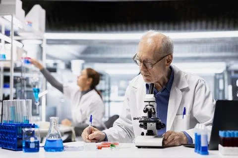 Senior scientist inspecting compound under microscope, reporting findings Stock Photos