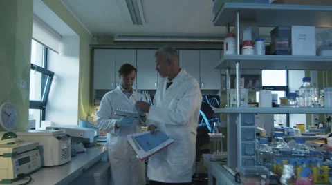 Senior scientist is walking with documents in a laboratory with colleagues Stock Footage