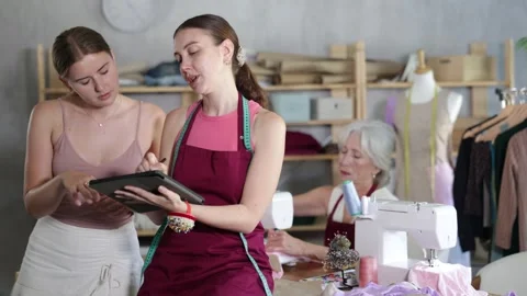 Senior seamstress sewing, apprentice with tablet accept order and talking with Video stock 318434592
