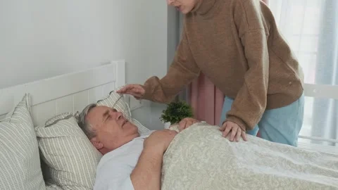 Senior sick man lying in a bed with fever and flu. Worried adult daughter caring Stock Footage 271253079