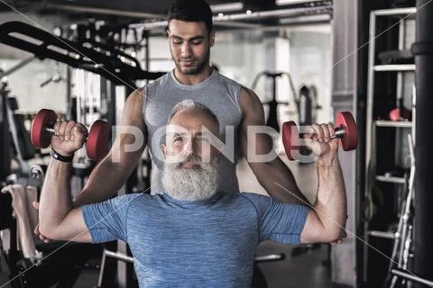 Senior sportsman doing exercises in athletic center with his instructor Stock Photos