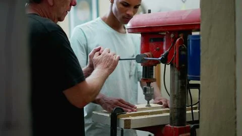 Senior staff guiding carpentry apprentice to use machine at workshop. Candi.. 스톡 사진