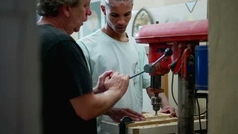 Senior staff guiding carpentry apprentice to use machine at workshop. Candi.. Stock Photos