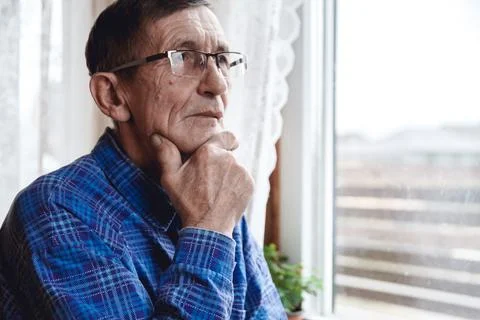 Senior standing at the window and thinking about something or fo Stock Photos