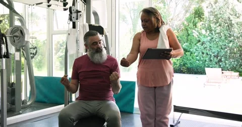 Senior trainer and client performing biceps curls on bench after reviewing Stock Footage 341936703
