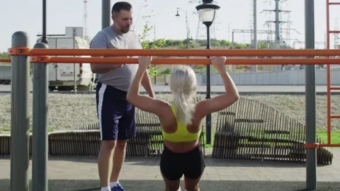 Senior trainer train her young female athlete to pulls herself up on the Stock Footage 143505273