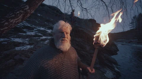 Senior Warrior in Chainmail Standing with Torch and Axe near River at Night Stock Footage 295535157