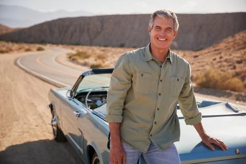 Senior white man leaning on open top car at desert roadside Stock Photos
