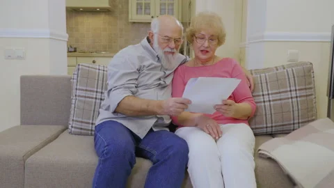 Senior woman and senior man checks their rent bills sitting on sofa at home Stock Footage