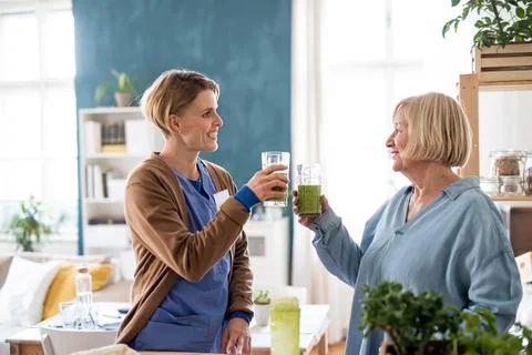 Senior woman with caregiver or healthcare worker indoors, drinking healthy Stock Photos
