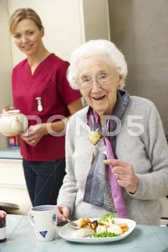 Senior woman with carer eating meal at home Stock Photos