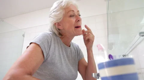Senior Woman Checking Skin In Bathroom Mirror Stock Footage