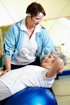 Senior woman doing abdominal exercises with her instructor in gym Stock Photos