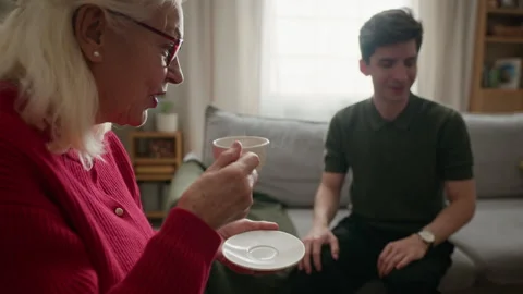 Senior Woman Drinking Tea and Talking with Male Caregiver at Home Stock Footage 340976341
