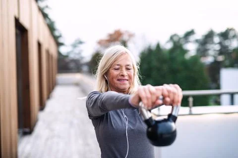A senior woman with earphones and kettlebell outdoors doing exercise. Stock Photos