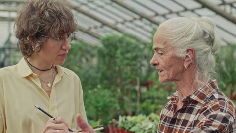 Senior Woman Explaining Work Tasks to Young Apprentice in Greenhouse 스톡 동영상 321645581