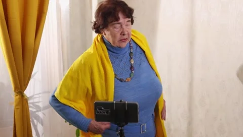 Senior woman filming exercise tutorial on smartphone while doing stretching 動画素材 334535631