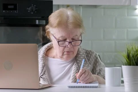 Senior woman in glasses working using laptop at home, writes with pen in Stock Photos