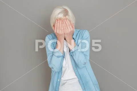 Senior woman in jeans jacket studio isolated on grey wall crying unhappy Stock Photos