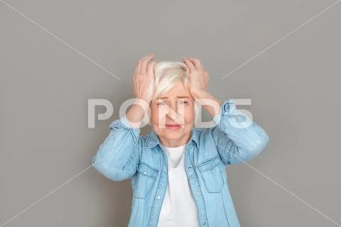 Senior woman in jeans jacket studio isolated on grey wall unhappy with headache Stock Photos