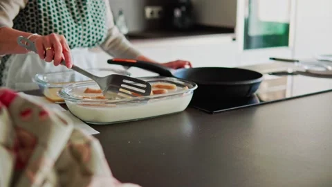 Senior woman on the kitchen soaking bread in milk and egg to make torrijas Stock Footage 261758223