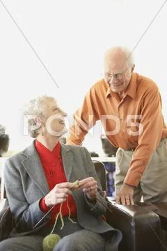 Senior woman knitting while husband watches Stock Photos