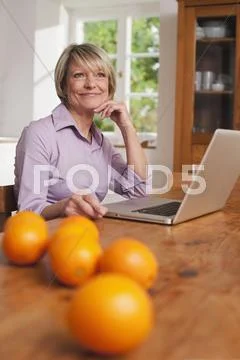 Senior Woman With Laptop And Fruits On Table In Foreground