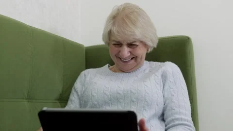 Senior woman laughing while using tablet on green sofa Vidéo 321856121