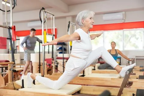 Senior woman performs exercise on reformer to improve coordination, balance, and Stock Photos