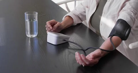 Senior woman placing cuff, tapping monitor, checking blood pressure at dining Stock Footage 338356271
