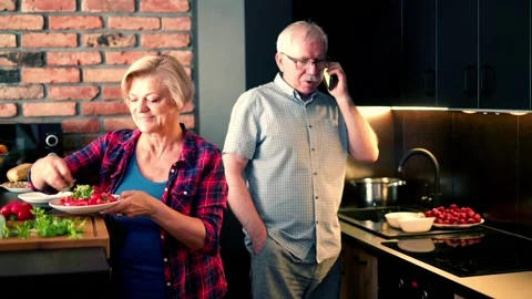 Senior woman preparing salad while her husband talking on cellphone Stock Footage 104550360