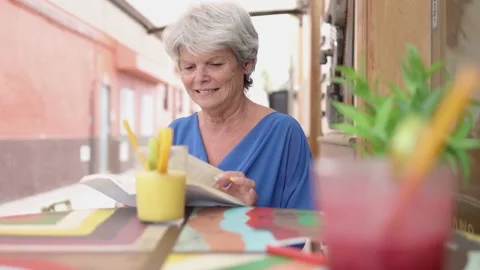 Senior woman reading a book while drinking healthy smoothie outdoor at bar Video stock 168251753