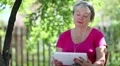 Senior woman sits on the chair in garden and funny uses white tablet computer HD Footage