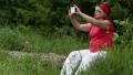 Senior woman sits on a fallen tree in the forest and makes photos on smartphone HD Footage
