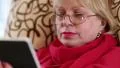 Senior woman sits on a sofa and uses electronic book. Woman reads a book HD Footage