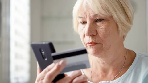 Senior woman sitting at home. Shopping online with credit card on smartphone Stock Footage