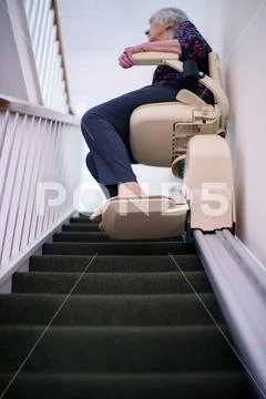 Senior Woman Sitting On Stair Lift At Home To Help Mobility Stock Photos