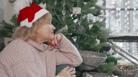 Senior woman smiling to the camera while sitting near Christmas tree at home Stock Footage 147463214