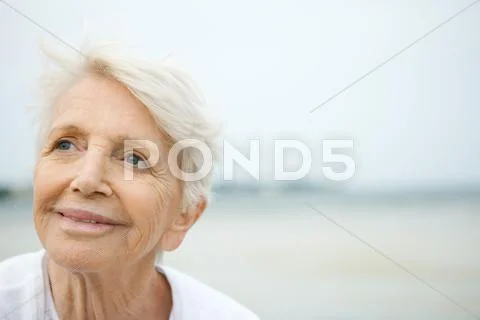 Senior Woman Smiling, Looking Up, Beach In Background