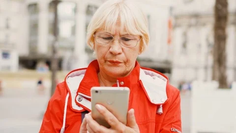 Senior woman standing outdoors using cellphone. Studying city map. Lost looking Stock Footage