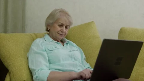 Senior woman thinking while using laptop on sofa at home Stock Footage 329244144