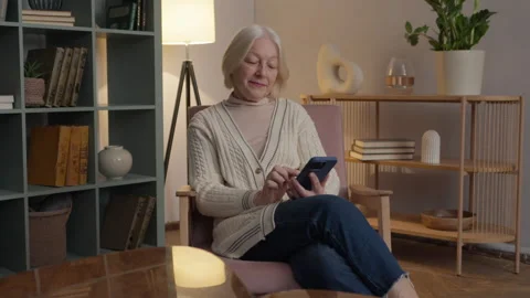 Senior Woman Typing Text Message On Smartphone While Sitting At Home Stock Footage 334716581